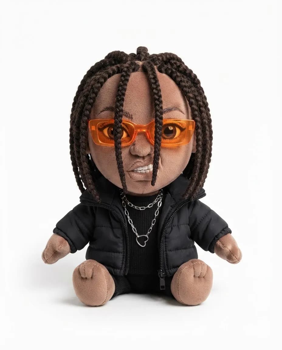 Collectible plush doll of a person with yarn braids, orange sunglasses, a black puffer jacket and chain necklaces, photographed on a white background