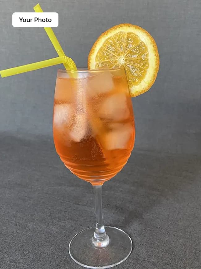 Phone photo of an iced orange drink in a wine glass on a grey surface