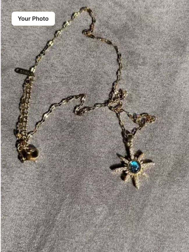 Plain phone photo of a gold chain necklace with a blue star pendant on grey fabric
