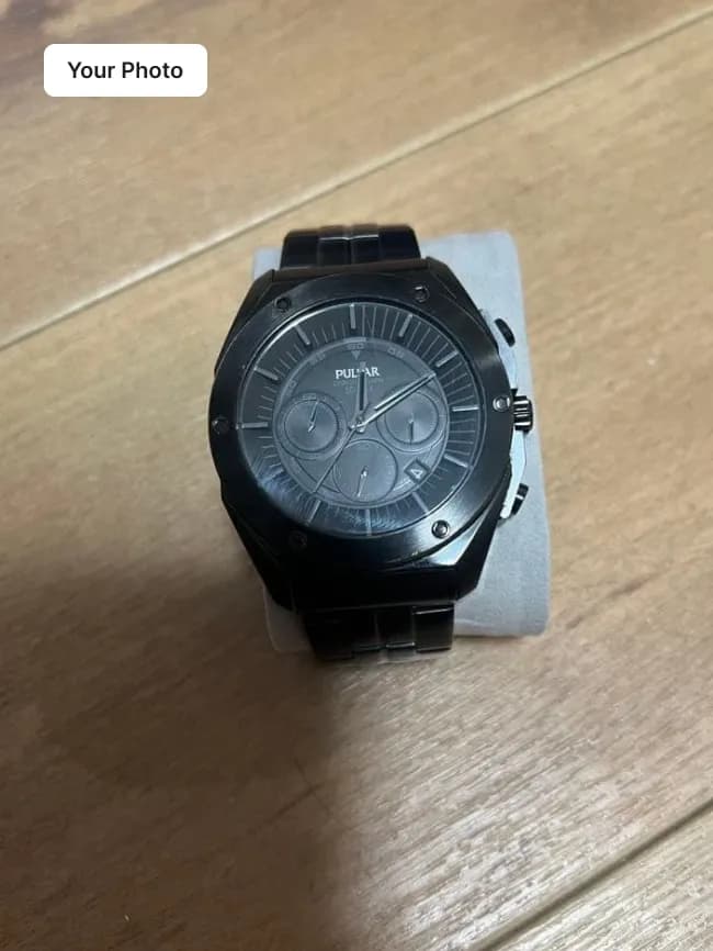Plain phone photo of a black chronograph watch on a wooden floor