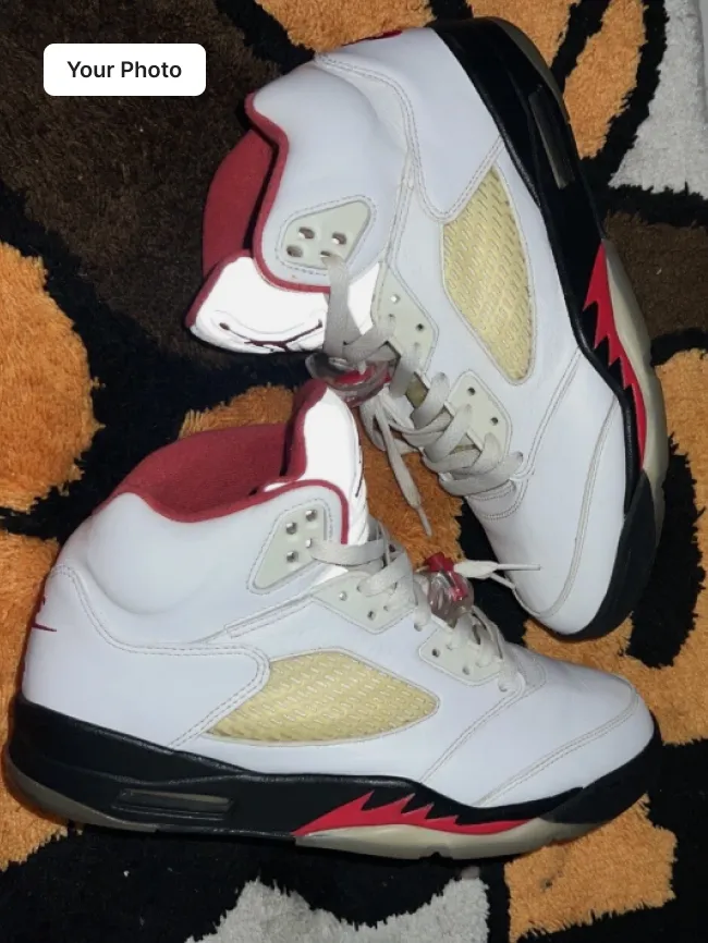 Plain phone photo of a white and red high-top sneaker on a patterned rug